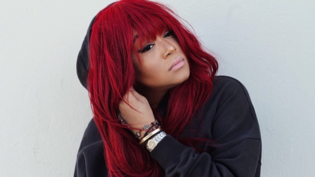 Tiffany Red in a black hoodie against a white wall