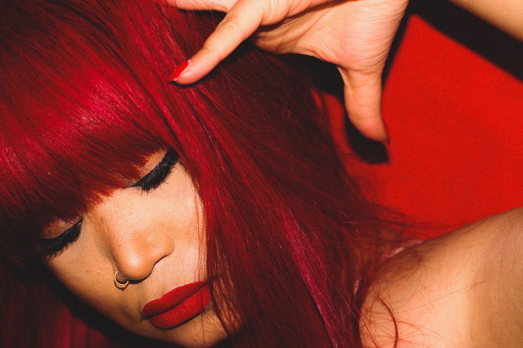Tiffany Red in close-up, red hair falling across her face against a red backdrop