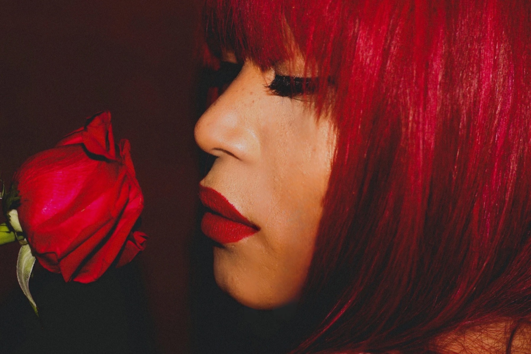Tiffany Red in profile, eyes closed, beside a red rose